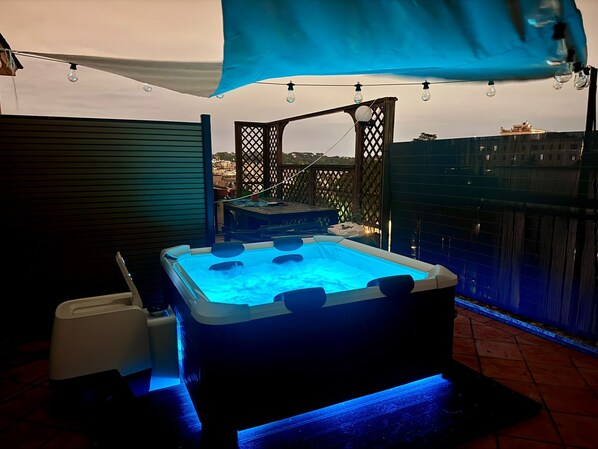 Ein Whirlpool mit blauem Licht, eine Holzterrasse und Blick auf die Stadtlandschaft.