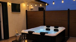 Un bain à remous avec une terrasse en bois, une table sur laquelle est posé un seau de champagne et des guirlandes lumineuses.