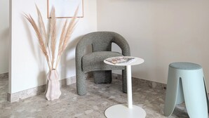 Habitació moderna amb televisió de pantalla plana, una cadira singular, una taula rodona petita i un vas amb plomes de plàtans.