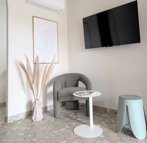 A modern room with a flat-screen TV, a unique chair, a small round table, and a vase with pampas grass. - Cosy studio with garden and jacuzzi 5 min from Avignon (Barbentane)