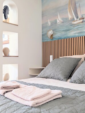 A bedroom with a bed, pillows, a painting of sailboats, a shell decoration, and a wooden slat headboard. - Cosy studio with garden and jacuzzi 5 min from Avignon (Barbentane)