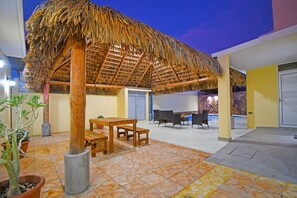 Eine Terrasse mit einem Reetdach, Holzmöbeln und Topfpflanzen.