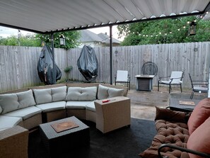 Eine überdachte Terrasse im Freien mit einer Eckcouch, einem kleinen Tisch und zwei Stühlen.