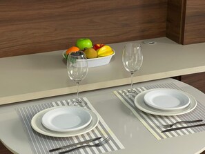 A dining table set with two plates, cutlery, and two wine glasses, with a fruit bowl on the side. - Unity 223 · Beachfront apartment in Cabo Branco for 3 people (João Pessoa)
