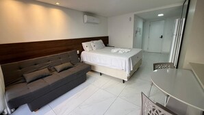 Ett modernt hotellrum med en bäddsoffa, en separat säng, ett matbord och en luftkonditioneringsanläggning.