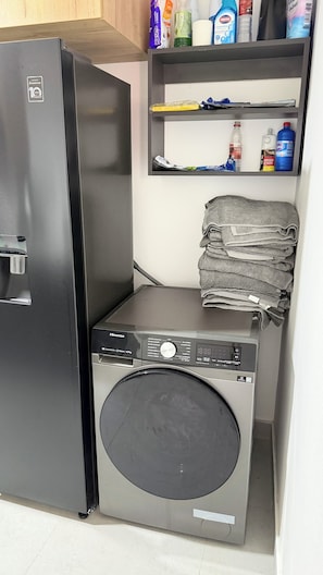 Una unidad compacta de lavadora-secadora con un panel de control, un dispensador de agua y un estante superior con productos de limpieza.