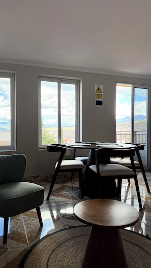 Una habitación con una mesa de comedor, sillas, un sofá y ventanas amplias con vistas.