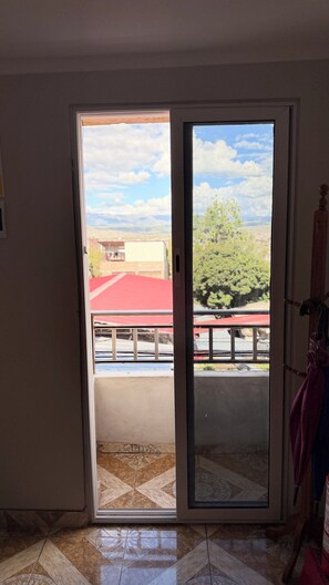 A room with a sliding glass door leading to an outdoor balcony with a red roof, a tiled floor, and a wooden chair. - Modern apartment in the heart of Huamanga, Ayacucho. (Ayacucho)