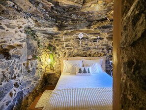A stone-walled bedroom with a bed, a hanging light fixture, and a decorative wall piece. - Cardenha das Formiguinhas | Cultural Heritage | Mountain | Nature (Monção)