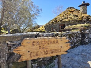 A wooden sign with carved text, a stone wall, and a stone house with a moss-covered roof. - Cardenha das Formiguinhas | Cultural Heritage | Mountain | Nature (Monção)