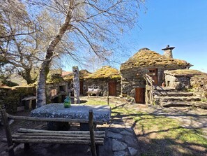 A rustic stone building with a thatched roof, a wooden bench, and a stone pathway. - Cardenha das Formiguinhas | Cultural Heritage | Mountain | Nature (Monção)