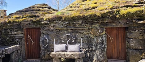 A stone building with a bed, two wooden doors, and a stone bench.