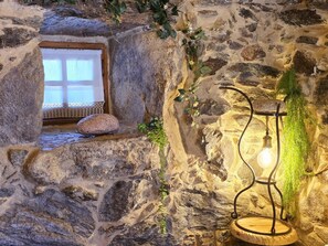 A stone wall with a small window, a hanging light fixture, and a rock on the ledge. - Cardenha das Formiguinhas | Cultural Heritage | Mountain | Nature (Monção)
