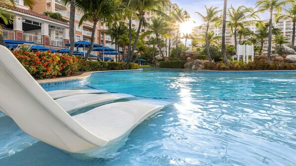 Una piscina con uno scivolo acquatico, circondata da palme e un edificio con balconi.