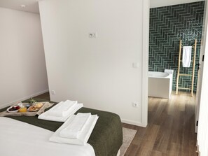 Ein Hotelzimmer mit Bett, Frühstückswagen, Pouf in Grün und einem Badezimmer mit Wandbelag in Fischgrätmuster.