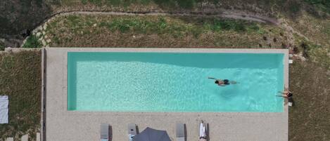 An aerial view of a rectangular swimming pool with clear water, surrounded by a concrete deck.