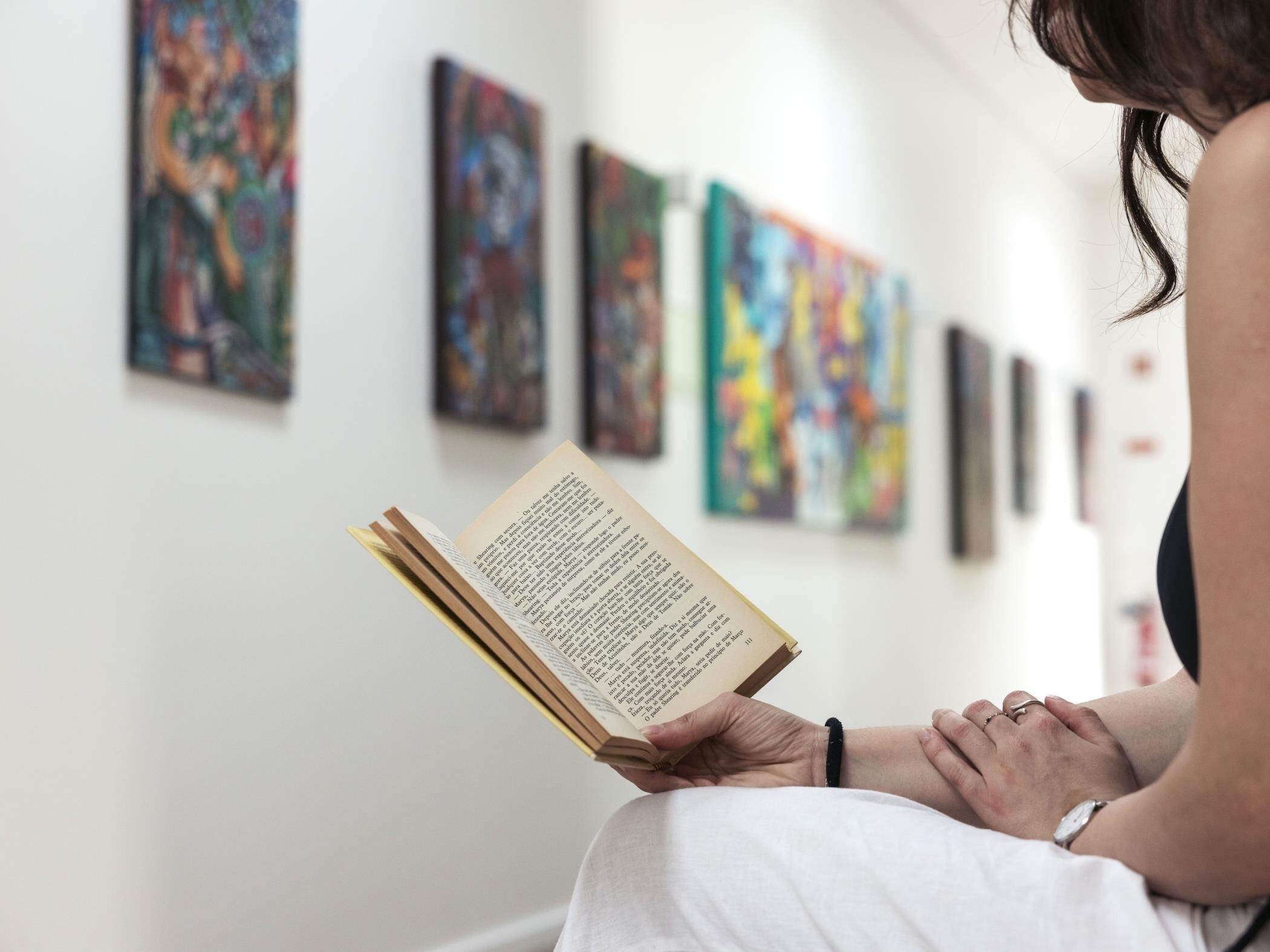 A person reading a book in a room with abstract paintings on the wall.