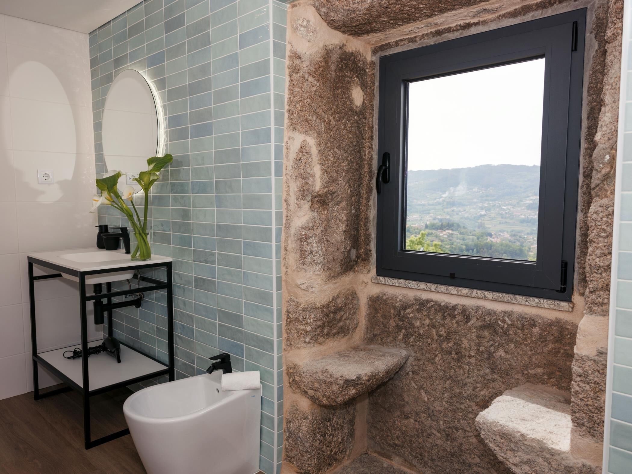 Ein Badezimmer mit Steinwand, einem Fenster mit Aussicht, einem weißen Waschbecken und einer Badewanne.