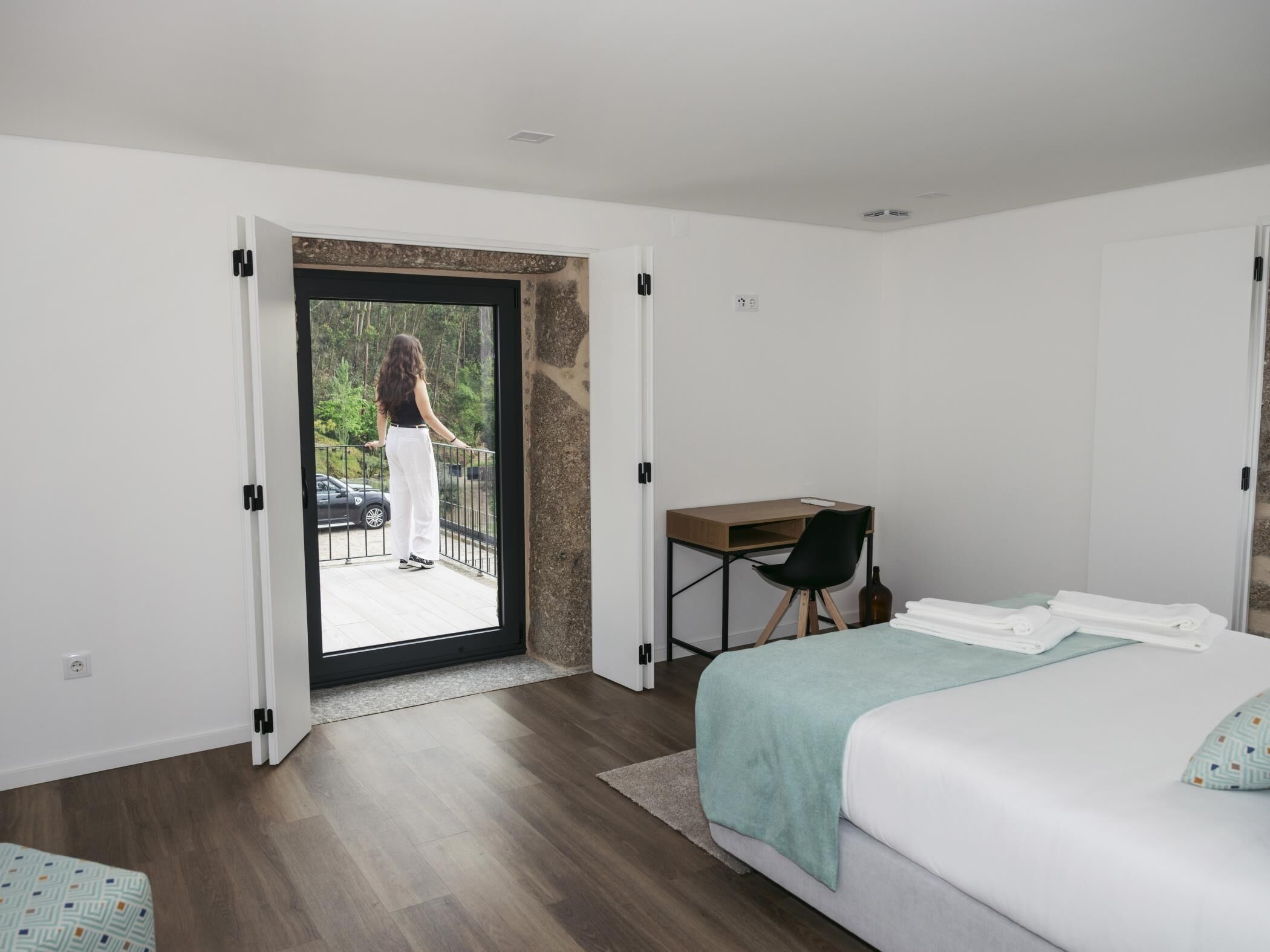 A bedroom with a bed, a desk, and a balcony.