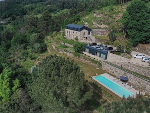Ein modernes Gebäude mit Steinaußenwand, einem Schwimmbecken und einem Parkplatz, umgeben von dichtem Wald.