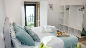 A bedroom with a bed, pillows, a bedside table with a tray of breakfast, a wardrobe, and a window with a view. - Cerca da Milhera | Suite 1 Nazaré | Country House | Swimming Pool | Minho (Ponte da Barca)