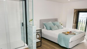 A modern bedroom with a glass shower enclosure, a bed with a view, and a breakfast tray on the bed. - Cerca da Milhera | Suite 1 Nazaré | Country House | Swimming Pool | Minho (Ponte da Barca)