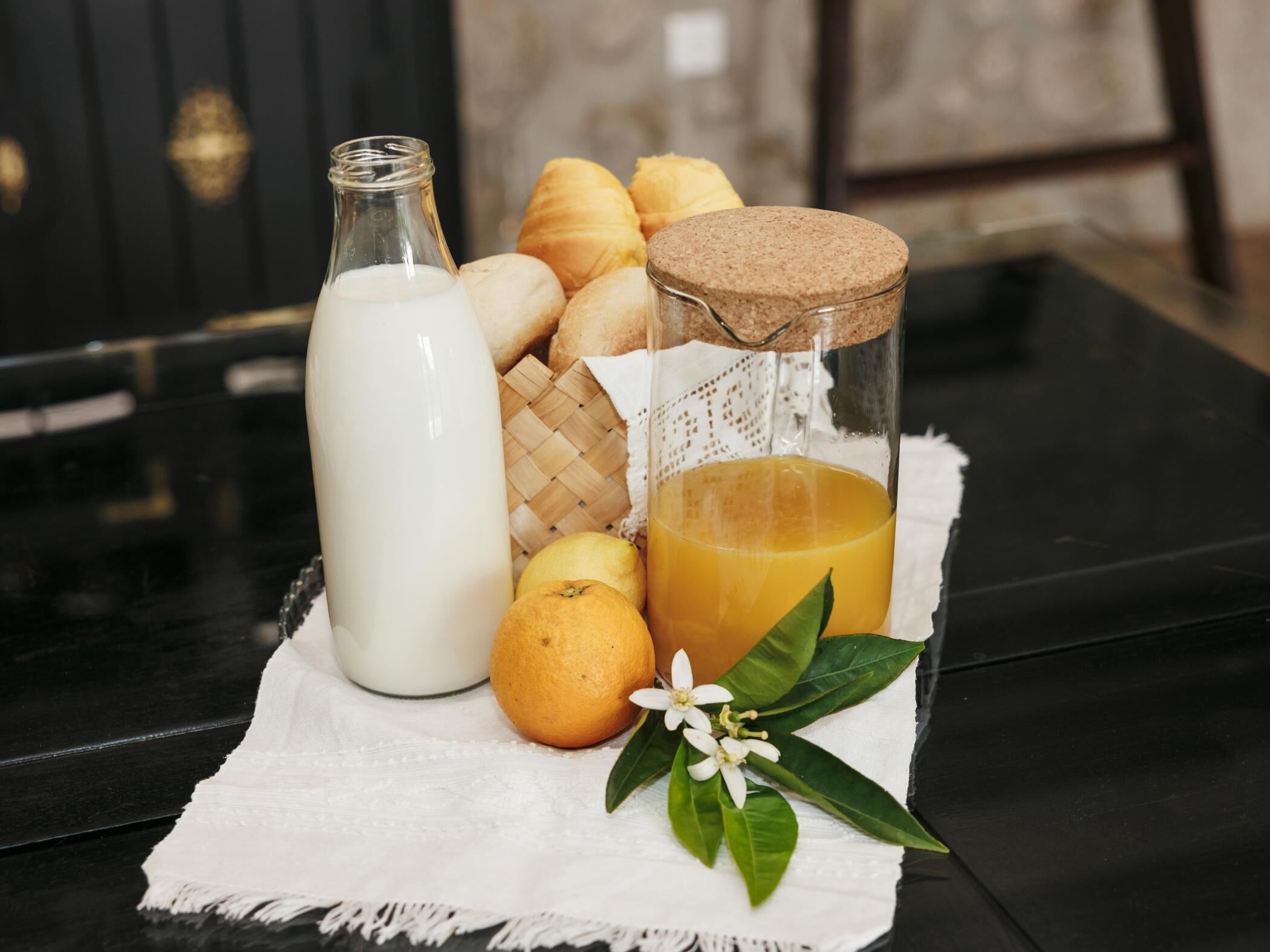 A bottle of milk, a glass of orange juice, a loaf of bread, a lemon, and a sprig of mint on a table.