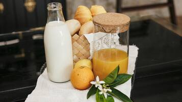 A bottle of milk, a glass of orange juice, a loaf of bread, a lemon, and a sprig of mint on a table.