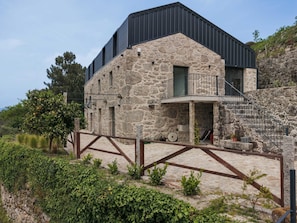 Un edifici de pedra amb una ampliació moderna, una tanca de fusta i una escala que porta a un balcó.