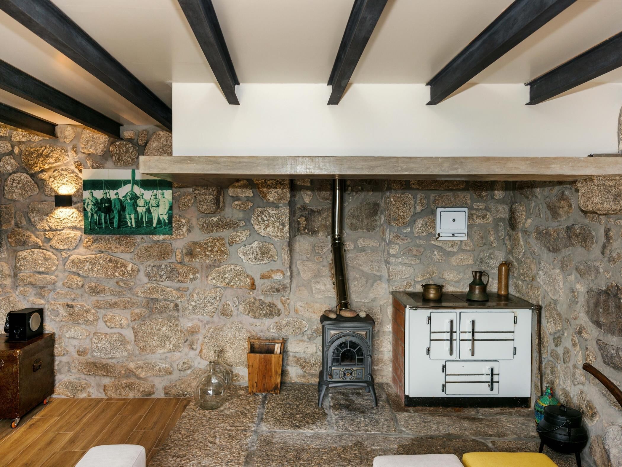 A stone-walled room with a wood-burning stove, a white cabinet with metal handles, and a vintage radio on a wooden cabinet.