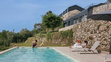 Une piscine avec des chaises longues, un mur en pierre et un bâtiment moderne en arrière-plan.