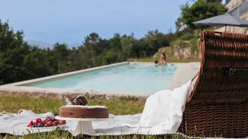 Un décor en bord de piscine avec une chaise en osier, un gâteau sur un présentoir et une couverture sur l’herbe.