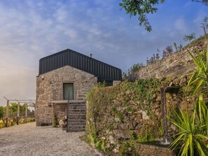 Un bâtiment en pierre au design moderne, avec un escalier menant à l’entrée et un mur en pierre naturelle agrémenté de végétation.
