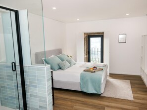 Ein Schlafzimmer mit Bett, einer Glasdusche, einem Fenster mit Aussicht und einem Nachttisch mit Tablett.