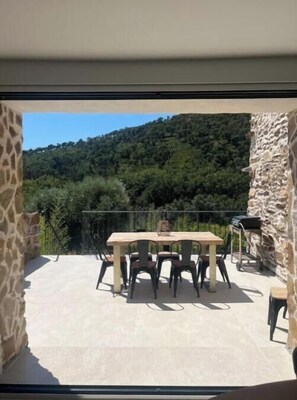 A balcony with a table and chairs, a stone wall, and a view of a forested hill. - Completely renovated haven of peace swimming pool (Grimaud)