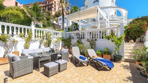 A patio with wicker furniture, a table, and lounge chairs. - Villa Las Chicas the authentic Andalusian retreat (Fuengirola)