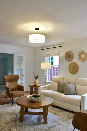 A living room with a sofa, armchair, round coffee table, and a hanging light fixture.