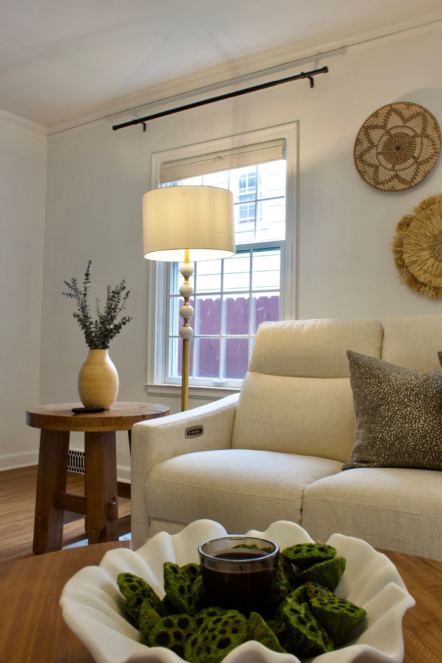 A living room with a sofa, a lamp, a vase with plants, and a decorative wall piece.