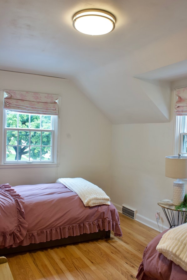 A bedroom with a single bed, a window with a view of trees, a radiator, and a lamp on a side table.