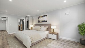 Un dormitorio moderno con una cama grande, mesitas de noche, una lámpara de noche, una planta en maceta y un cuadro en la pared.