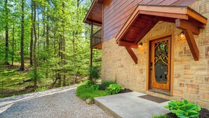 Eine rustikale Holzhütte mit Natursteinfassade, einer Holzveranda und einer Schotterauffahrt, die zu einem bewaldeten Gebiet führt.
