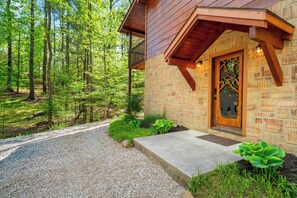 Eine rustikale Holzhütte mit Natursteinfassade, einer Holzveranda und einer Schotterauffahrt, die zu einem bewaldeten Gebiet führt.