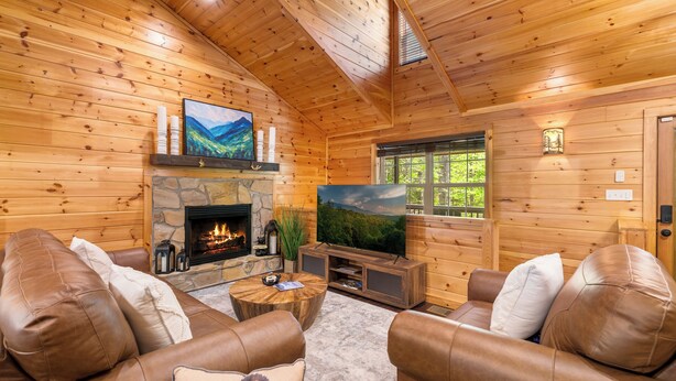 Ein Holzblockhaus-Interieur mit Kamin aus Stein, Ledersofas, einem Fernseher und einer Wand als Steinakzent.
