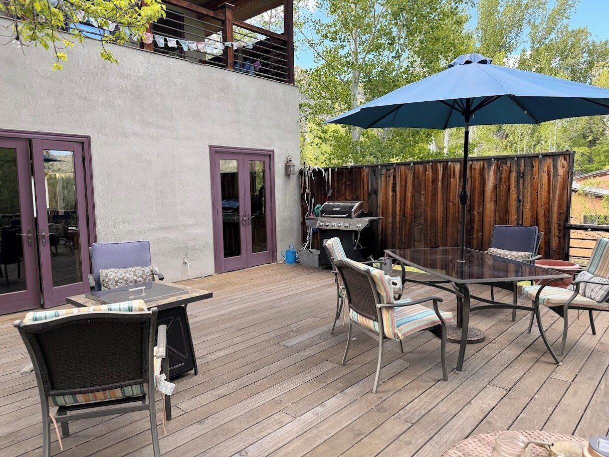 An outdoor patio with a glass table, wicker chairs, and a blue umbrella.