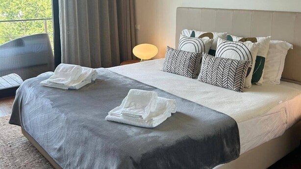 Ein Hotelzimmer mit einem großen Bett, einem Nachttisch, einer Lampe und Blick auf Grünflächen.