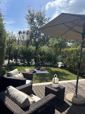 Eine Terrasse im Freien mit Korbmöbeln, einem weißen Sonnenschirm und einem kleinen Tisch.