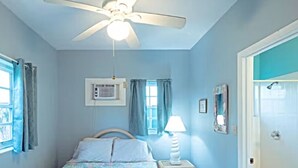 Ein Schlafzimmer mit Bett, Deckenventilator, Nachttisch mit Lampe und einem Badezimmer mit Toilette.