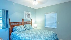 Ein Schlafzimmer mit Bett, Deckenventilator, Klimaanlage und einem Fenster mit Jalousien.