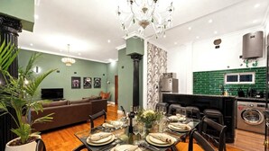 Ein modernes Wohnzimmer mit Essbereich, einer Couch, einer Kristallleuchtre und einer Küche mit grüner Rückwand.