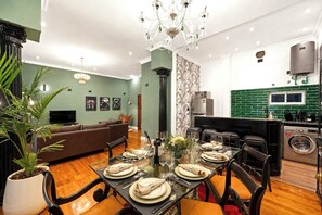 A modern living room with a dining area, a sofa, a chandelier, and a kitchen with a green backsplash. - Bold Designer Apartment near Puerto Madero (Buenos Aires)